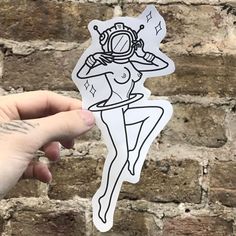 a person holding up a sticker in front of a brick wall with a drawing on it