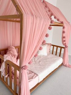 a pink canopy bed with pom poms on it