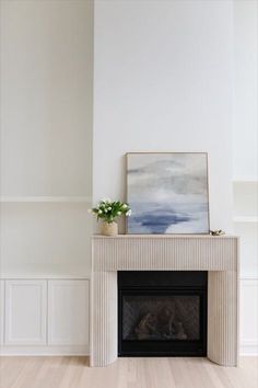 a white fireplace with a painting on the mantle and potted plant next to it