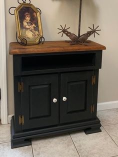 a black cabinet with a painting on the top and two metal birds sitting on it