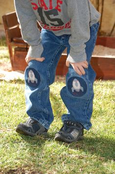 a young child standing in the grass with his hands on his knees wearing jeans and shoes