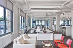 an office with white couches, red chairs and tables in front of large windows