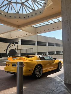 a yellow sports car is parked in front of a building with a circular sculpture on it's side