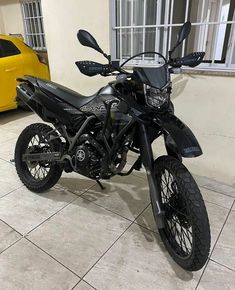 a black motorcycle parked next to a yellow car in a room with tile flooring