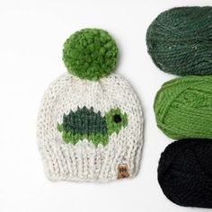 three knitted hats with green and black pom - poms