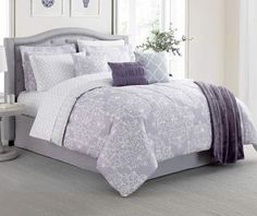 a bed with white and purple comforters on top of it in a room next to a window