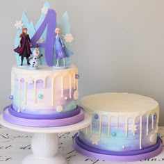 two cakes decorated with frosting and frozen princess figures, one is white and the other has purple icing