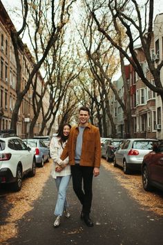 a man and woman are walking down the street in front of parked cars on both sides