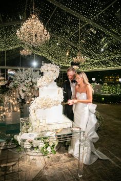 a bride and groom cutting their wedding cake at the end of an indoor venue with chandeliers overhead