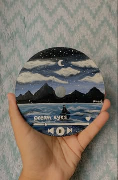 a person holding up a painted disc with the ocean and mountains in the back ground