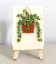 a miniature easel holding a potted plant with green plants growing out of it