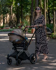 a woman is walking with her stroller in the park and she has sunglasses on