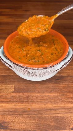 a spoon full of soup in a bowl on top of a wooden table next to a plate