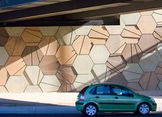 a small green car parked in front of a wall with geometric designs on it's side