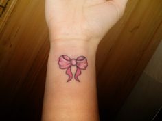 a woman's wrist with a pink bow tattoo on it