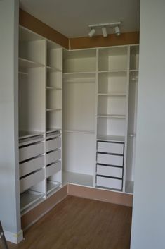 an empty walk in closet with white shelves and drawers on the wall, next to a wooden floor