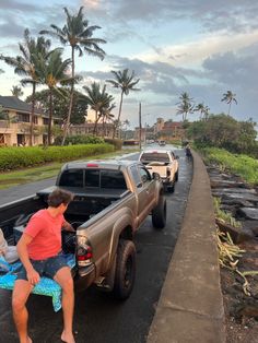 a man sitting on the back of a truck next to other cars and palm trees