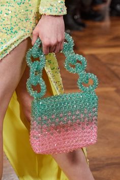 a woman's hand holding a pink and green beaded purse on top of a wooden floor