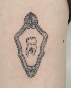 a tooth in a frame tattoo on the back of a woman's thigh,