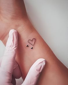 a person wearing gloves and holding their arm up to the wrist with a small tattoo on it