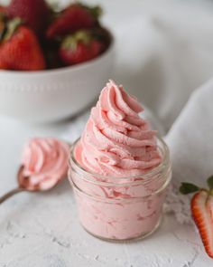 a small jar filled with pink whipped cream next to two strawberries on a table