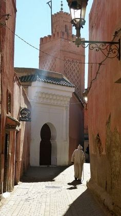 a man walking down an alley way in the middle of some old buildings with a clock on it