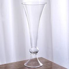 a clear vase sitting on top of a wooden table next to a white window curtain