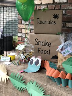 a table topped with paper cutouts and plants next to a sign that reads taranulasa's snake food