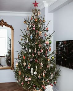 a small christmas tree with ornaments on it in a living room next to a mirror