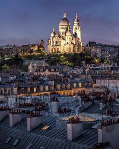 an old cathedral lit up at night in the distance, with rooftops and buildings below