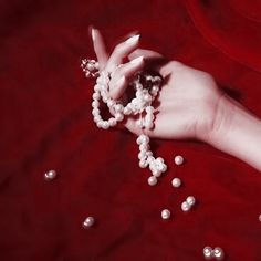 a woman's hand holding some beads on top of a red cloth with white pearls