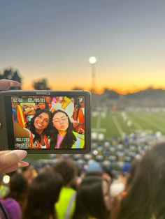 a person holding up a cell phone to take a photo at a football game with the sun setting in the background