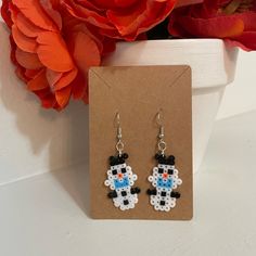 a pair of black and white beaded earrings on a brown card next to flowers