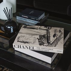 two books sitting on top of a glass table next to a vase and candle holder