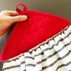 a hand holding a red piece of cloth next to a white and black striped skirt