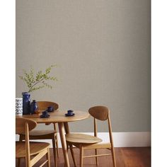 a wooden table with two chairs and a vase on it next to a wall that has a plant in it