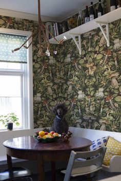 a small dog sitting at a table in front of a wallpapered dining room