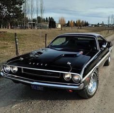 an old black muscle car parked on the side of a road in front of a fence