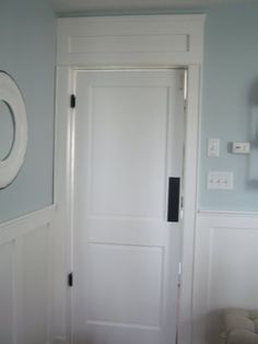 a white door in a blue room next to a chair and wall with two mirrors on it