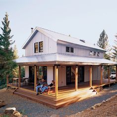 two people sitting on the porch of a small cabin style home with wraparound porches