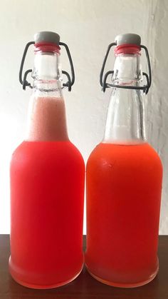 two glass bottles filled with liquid sitting on top of a wooden table