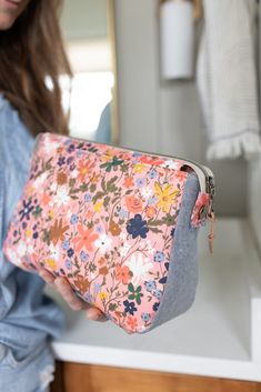 a woman is holding a flowered purse in her hand and looking at the mirror