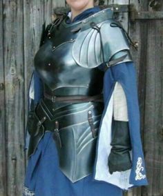 a woman in a blue and silver outfit standing next to a wooden fence with her hands on her hips