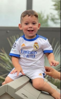 a little boy sitting on top of a bench wearing a soccer uniform and smiling at the camera