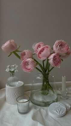 pink roses are in a vase on a white tablecloth with candles and other items