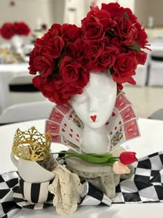 a table topped with a white vase filled with red roses and a crown on top of it