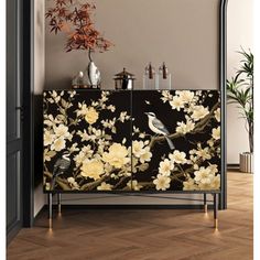 a black and white floral cabinet with birds on it, next to a potted plant