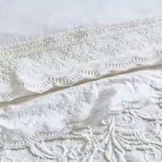 two white bedspreads are laying next to each other on a bed with lace