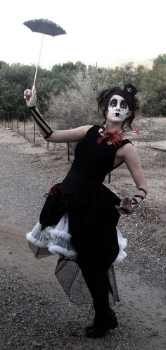 a woman dressed as a skeleton holding an umbrella in her hand while walking down a dirt road