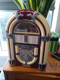 an old fashioned jukebox sitting on top of a wooden table next to a potted plant